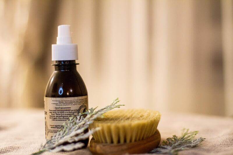 Na naturalnym materiale leżą gałązki, szczotka do masażu i arganowy olej kosmetyczny do pielęgnacji cery i skóry głowy.