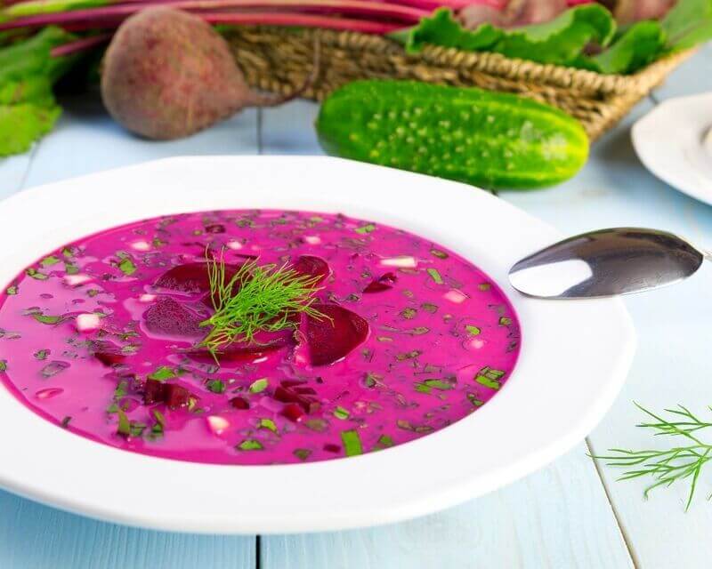 Na stole leży głęboki talerz z gotowym do jedzenia chłodnikiem buraczkowym ozdobionym koperkiem.