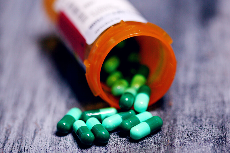 Na ławie leży otwarte opakowanie suplementu, z którego wysypały się kapsułki chlorelli.