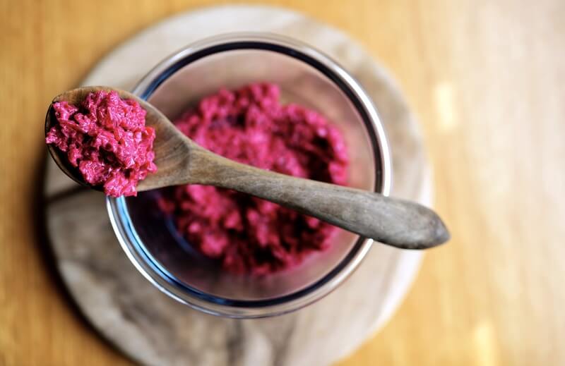 Na stoliku leży szklany słoik ze świeżą różową ćwikłą nabraną na drewnianą łyżeczkę.