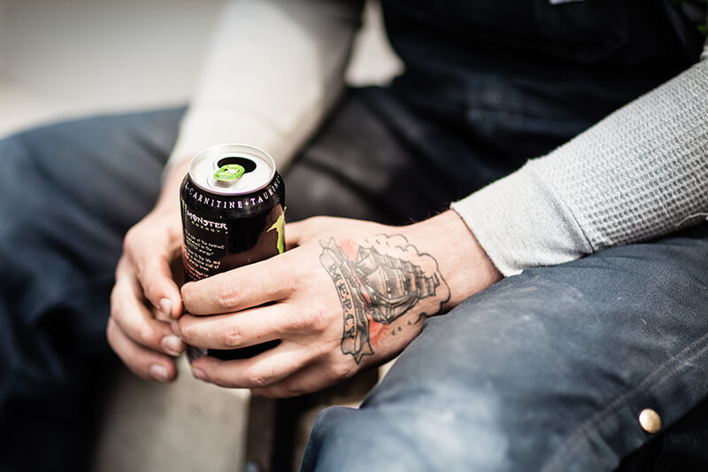 Mężczyzna trzyma w dłoniach napój energetyczny zawierający kofeinę, taurynę, L-karnitynę i inne substancje pobudzające organizm.