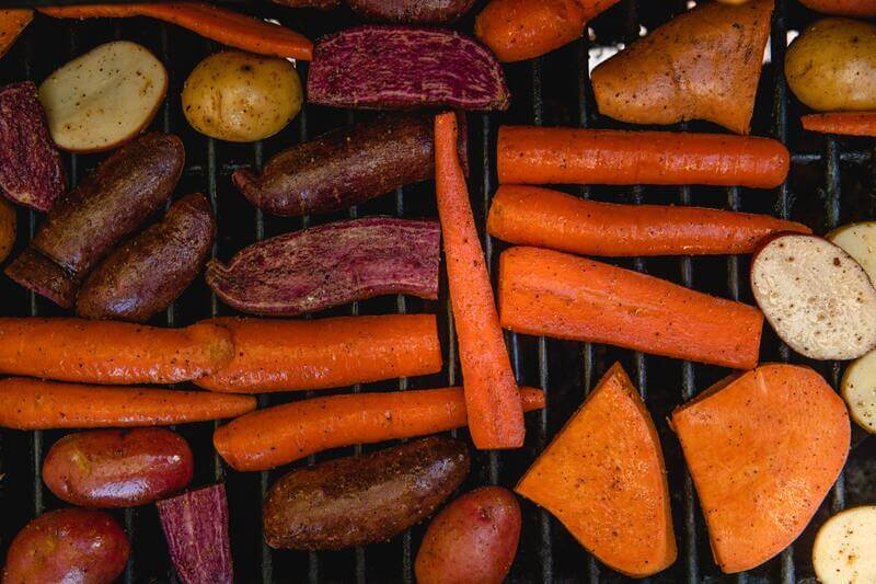 Na ruszcie leży wiele odmian ziemniaków, łącznie z różnymi kolorami batatów.