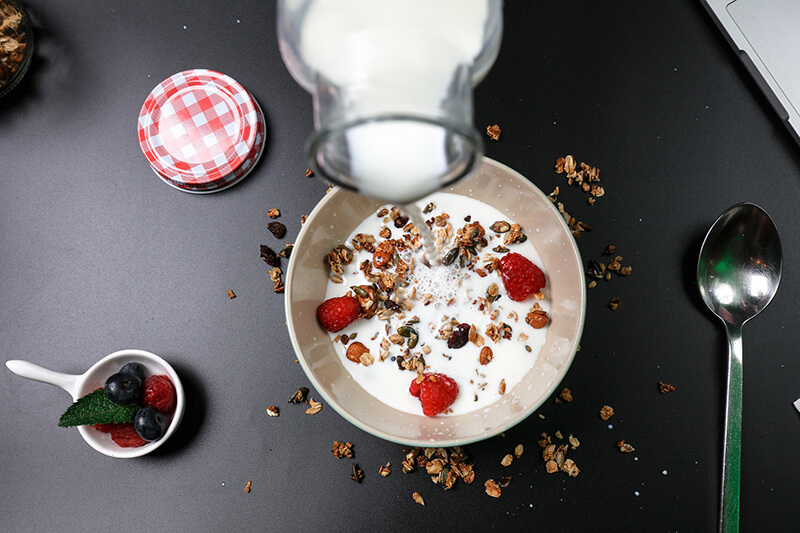 Do miski z płatkami, otrębami, owocami i orzechami wlewane jest świeże mleko bez laktozy idealne na śniadanie.