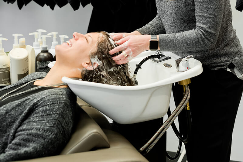 Kobieta leży u fryzjera na profesjonalnym fotelu do mycia włosów i ma wykonywany delikany masaż głowy z użyciem najlepszych preparatów naturalnych do włosów.