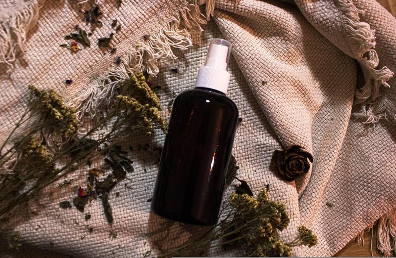 Naturalny olejek w ciemnej buteleczce chroniącej przed światłem leży na ściereczce z naturalnego surowca w towarzystwie suszonych roślin.