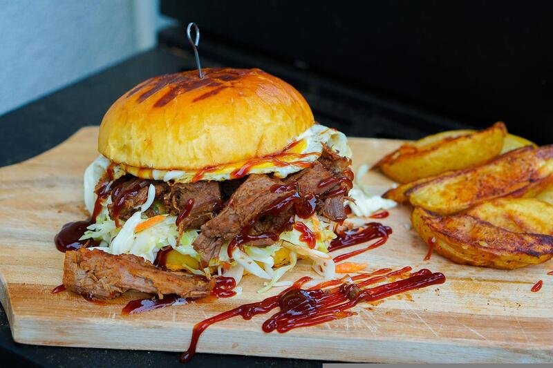 Burger przygotowany z bezmięsnej szarpanej wieprzowiny podano z sałatą i sosami.