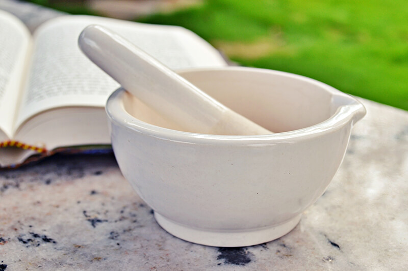 Na ławce obok książki medycznej leży moździerz do rozkruszania witamin i minerałów.