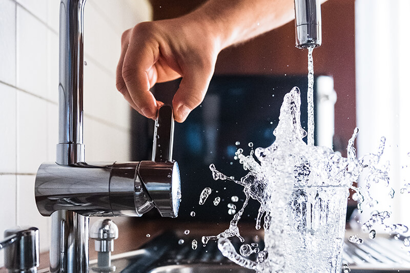 Mężczyzna odkręca kran w kuchni i leje do szklanki świeżą wodę, która mocno się rozchlapuje.