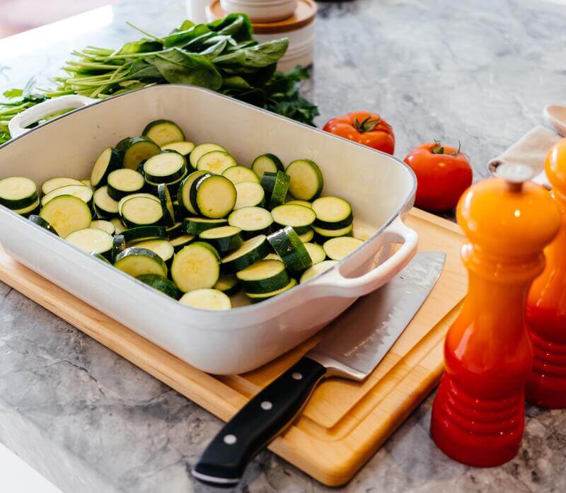 Do naczynia żaroodpornego na drewnianej desce wkrojono plasterki cukinii, do której doda się inne warzywa - pomidory, szpinak, przyprawy.