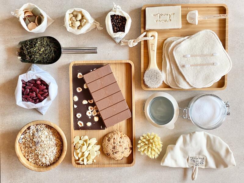 Na stole ułożono wiele ekologicznych gadżetów do domu: bambusowe tacki, wielorazowe przybory kosmetyczne, naturalne kosmetyki, płócienne woreczki z sypkimi artykułami spożywczymi, metalowe i szklane przybory.